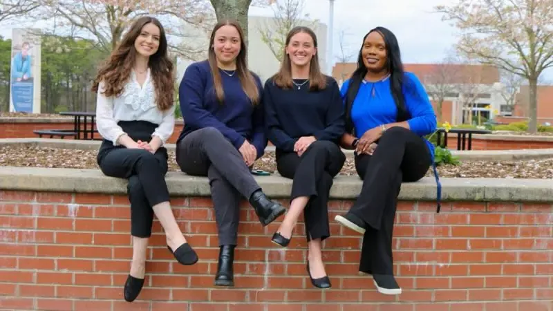 Four female students sitting on a low brick wall on campus